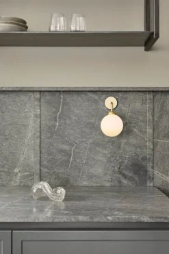 Nuura Apiales vägglampa, fast installation, borstad mässing - opalvit